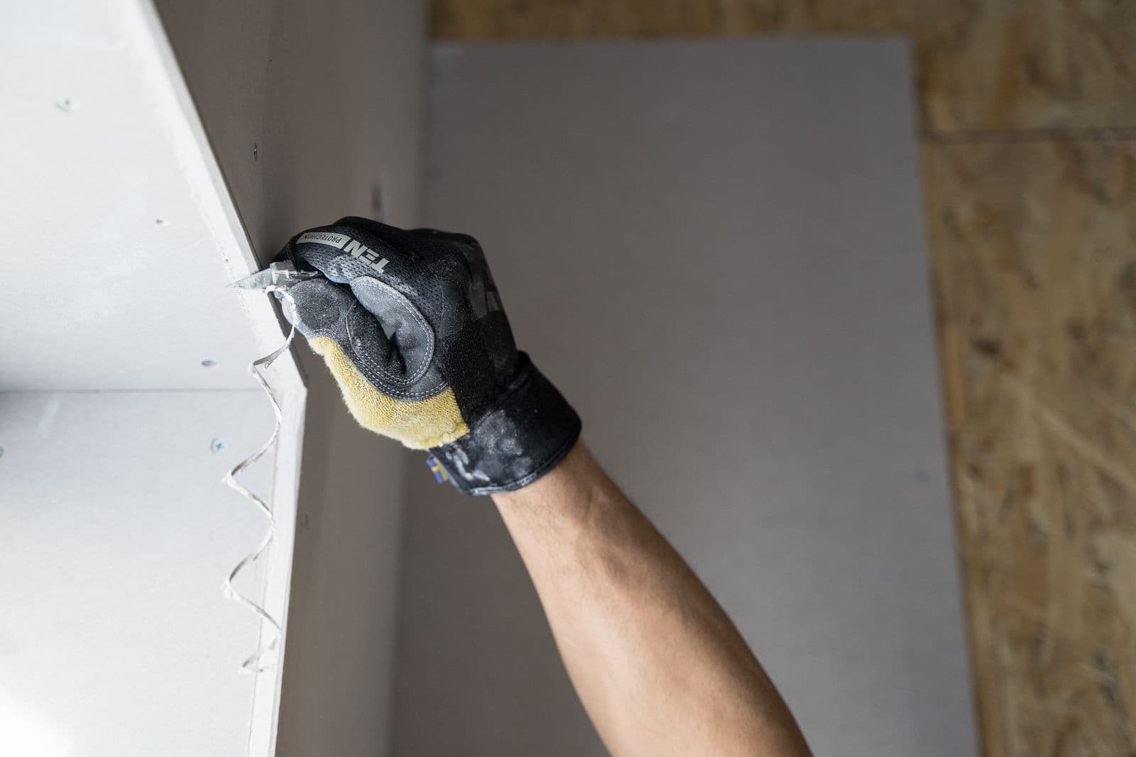 Close-up of a gloved hand finishing a drywall corner with a taping knife
