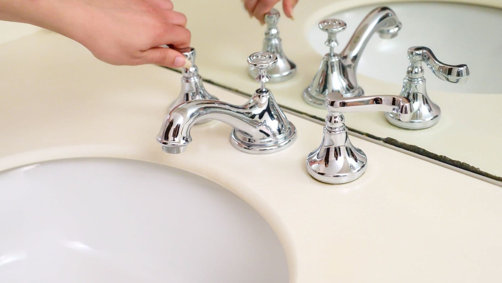 Hand adjusting a chrome bathroom faucet on a vanity sink